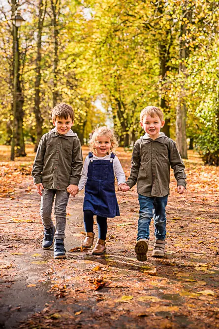 Outdoor Family Portrait of 3 young siblings walking with autumn leaves and trees behind them taken by Family Photographer Rebekah Morecroft