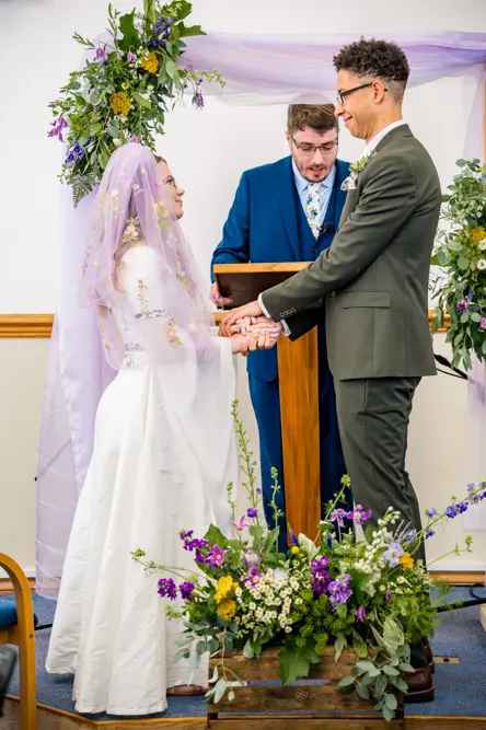 Bride and Groom holding hands at the front of the church with their Pastor standing behind the lectern.