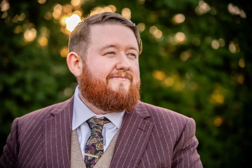 Groom standing in dappled winter sunlight through the trees at Everglades Hotel in Widnes, Cheshire