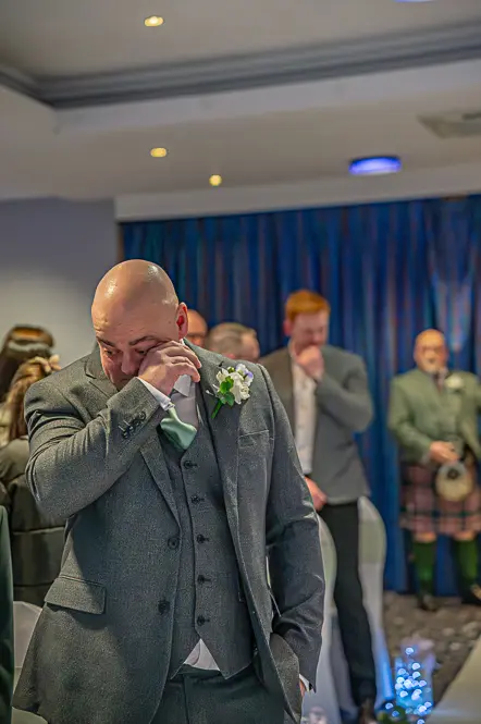 Groom wiping a tear away while waiting for bride to enter the room