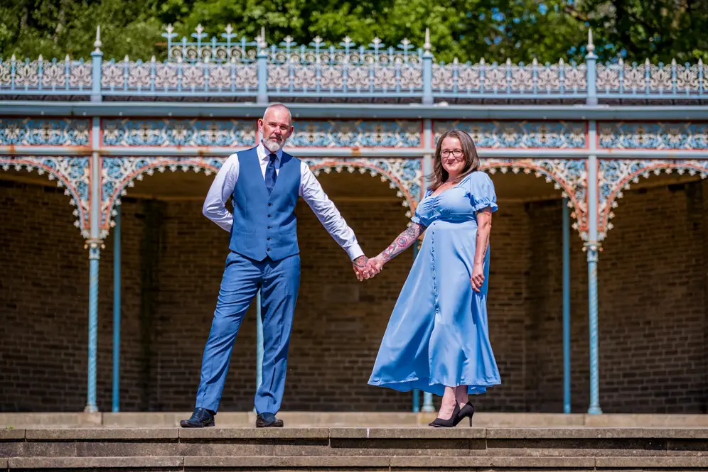 Couple standing apart but holding hands together with bandstand behind them