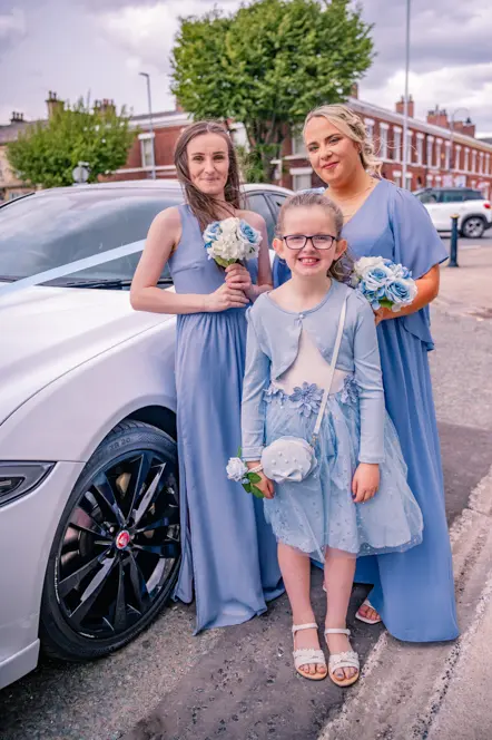 Bridesmaids and flower girl standing next to White Jaguar