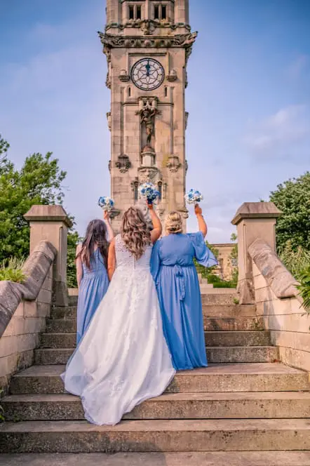 The backs of the bride and her two bridesmaids with their bouquets in the air while standing on some steps.