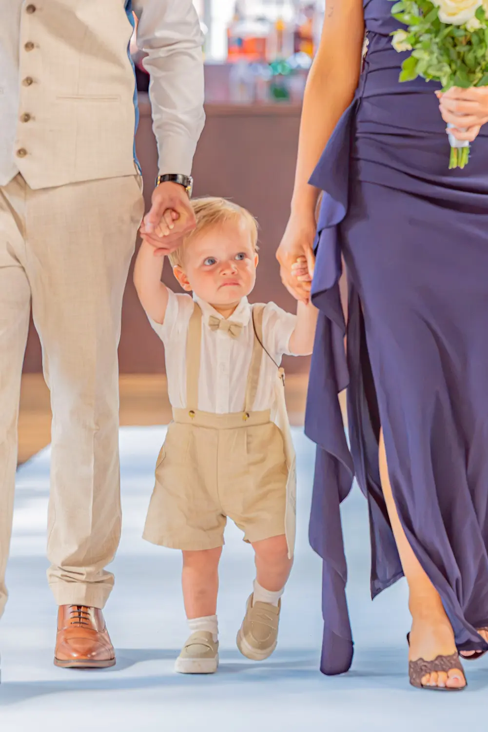 Page boy walking down the aisle holding hands with his parents