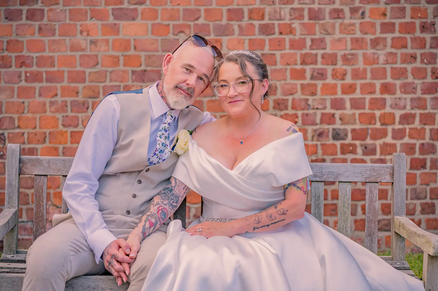 A relaxed portrait of the bride and groom sitting together on a wooden bench