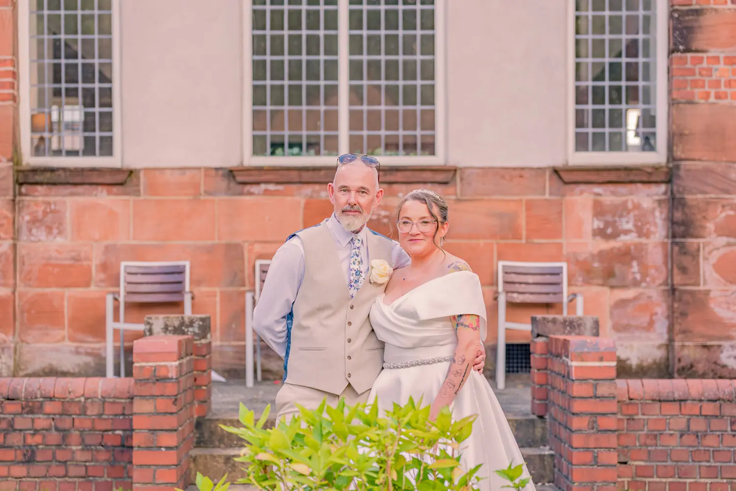 Wide landscape portrait of the bride and groom standing together in the stone courtyard