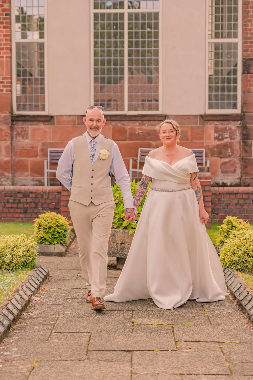 Relaxed portrait of the bride and groom walking hand in hand through the grounds, captured by The Old School Rooms wedding photographer