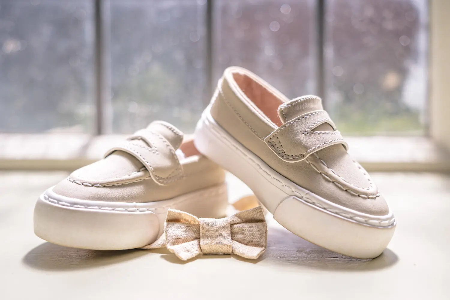 Detail photograph of a tiny pair of brown leather shoes and a cream bow tie