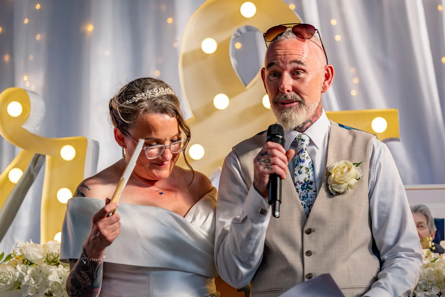 The groom standing to deliver his wedding speech with the bride smiling by his side