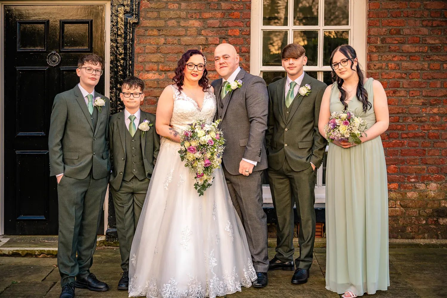 Bride and groom standing outside a historic Georgian brick building with their three sons and daughter.