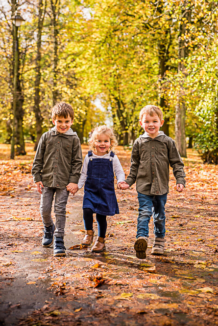 Three young siblings walking through autumn leaves, family photographer