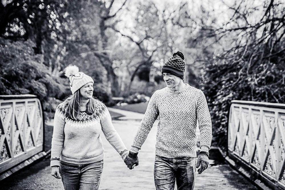 Black and White Outdoor Family Portrait of couple walking while holding hands and wearing hats and gloves