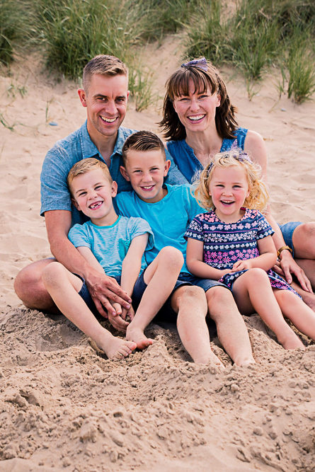 Outdoor Family Portrait of family of 5 seating on the beach laughing and smiling