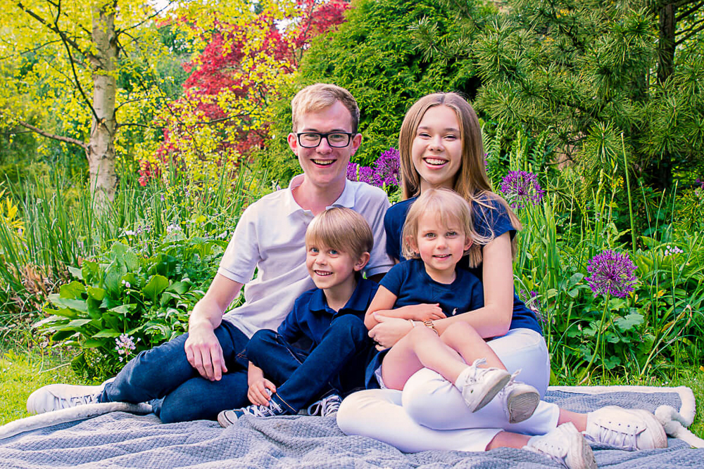 Outdoor Family Portrait of 4 siblings seating a blanket with flowers and trees behind them