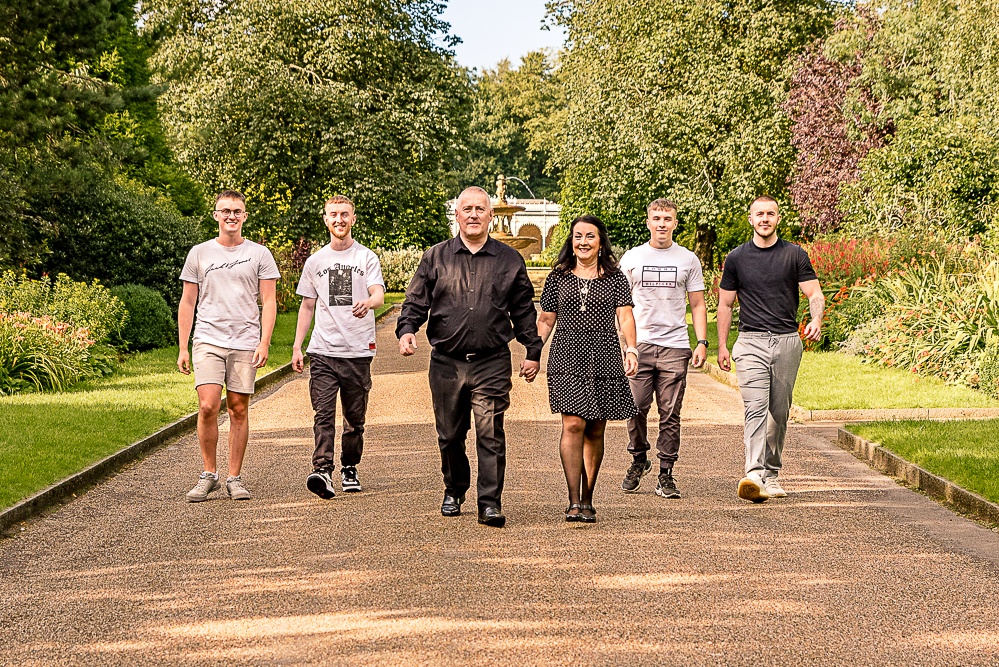 Outdoor Family Portrait of family of 6 walking. Parents holding hands slightly in front 4 young adult sons