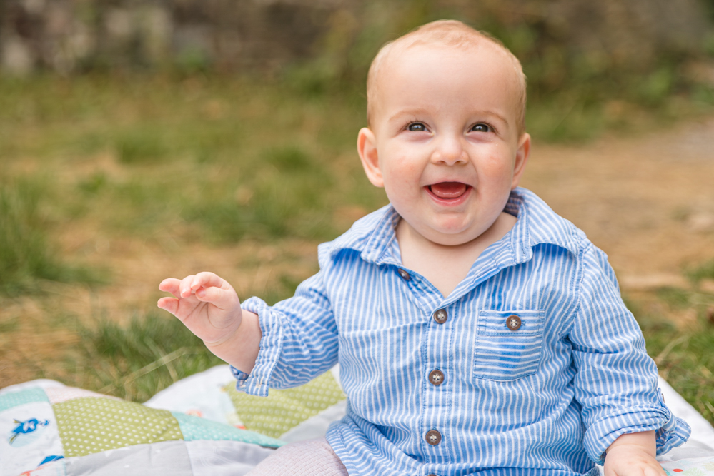 Baby boy smiling while sitting on a blanket, outdoor portrait session