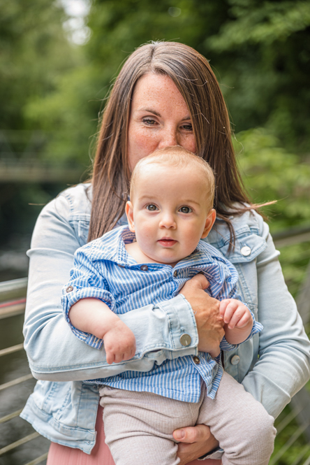 Outdoor Family Portrait of Mum holding baby boy and kissing the back of his head