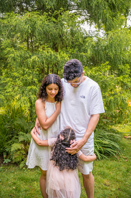 Outdoor Family Portrait of parents looking down at young daughter.