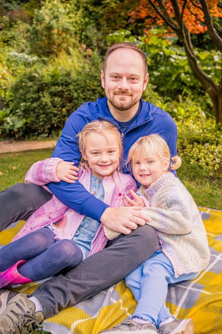 Outdoor Family Portrait of father and 2 young daughters cuddling