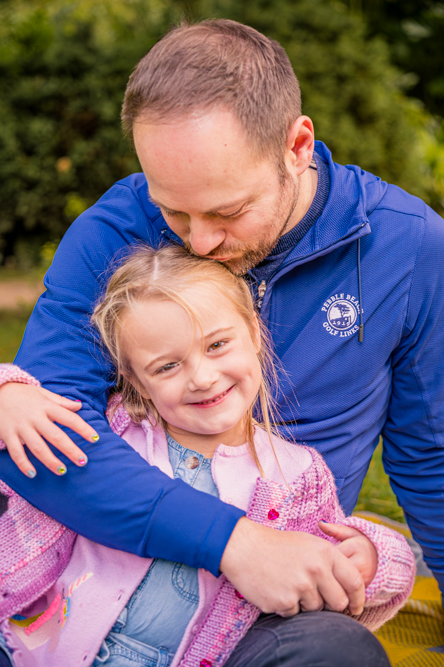 Outdoor Family Portrait of father and young daughter. Father is cuddling and kissing daughter's head.