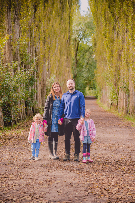 Outdoor Family Portrait of family of 4 standing with large trees around the edges