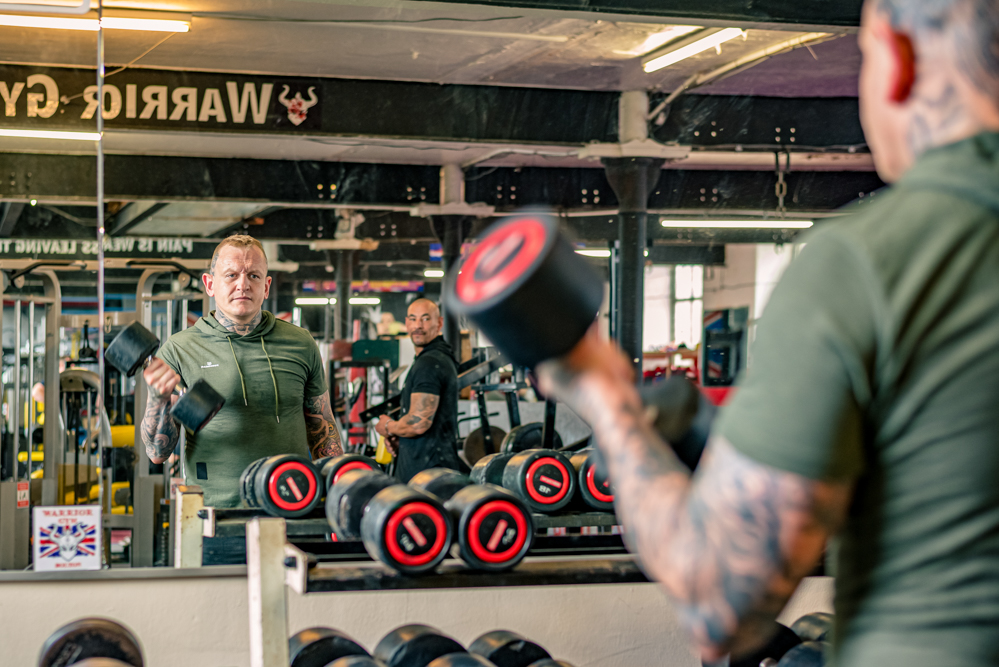 Man lifting weight while looking into his reflection.