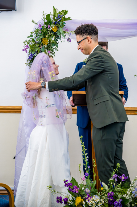 Groom lifting the bride's purple veil during their wedding ceremony at Peel Street Baptist Church