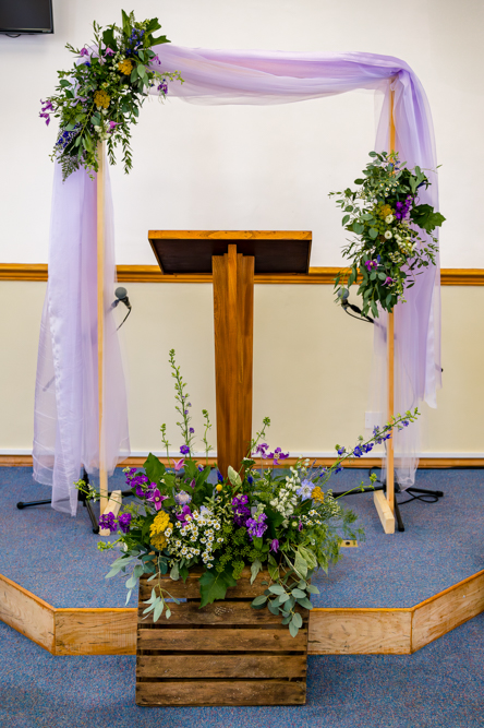 Stage at Peel Street Baptist Church decorated for the wedding ceremony with purple cloth and wild flower arrangements
