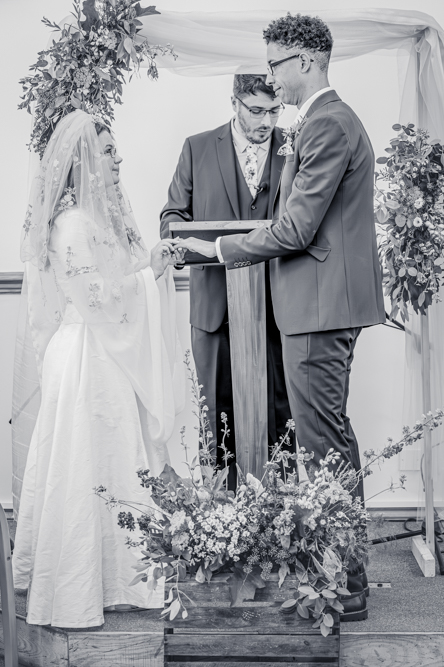 Black and white image of Bride placing the Groom's his ring on his finger.