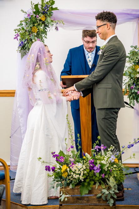 Bride and Groom holding hands at the front of the church with their Pastor standing behind the lectern.