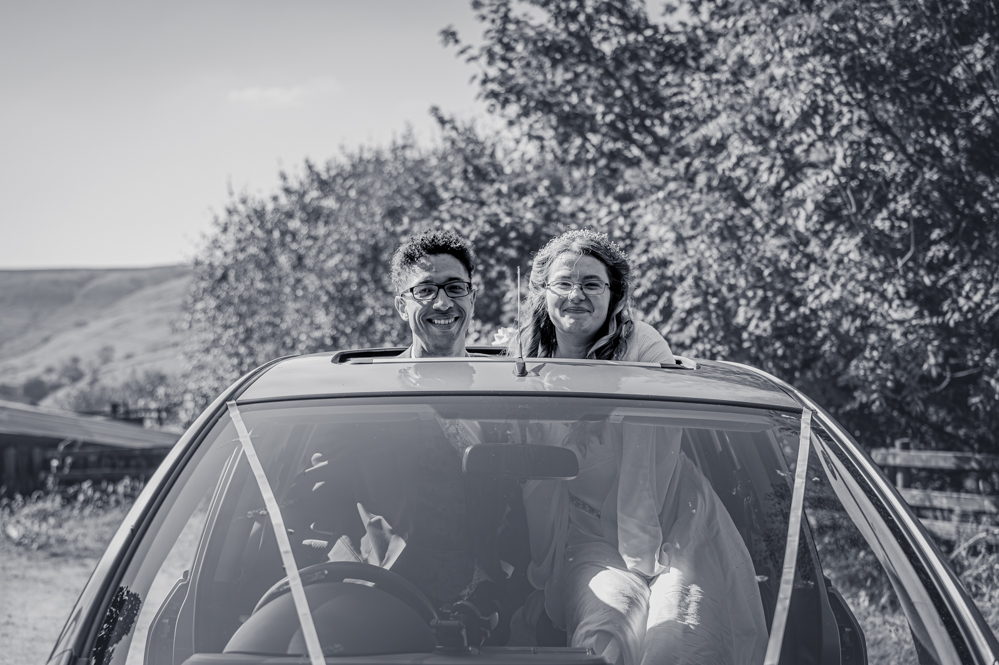 Bride and groom poking their heads through the sunroof of their wedding car on arrival at Cronkshaw Fold Farm, Rossendale