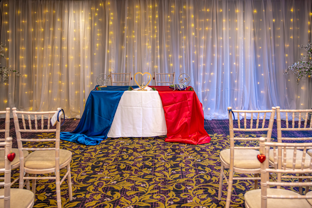 Table decorated with blue, white and red cloth and wooden heart at the centre ready for a wedding.