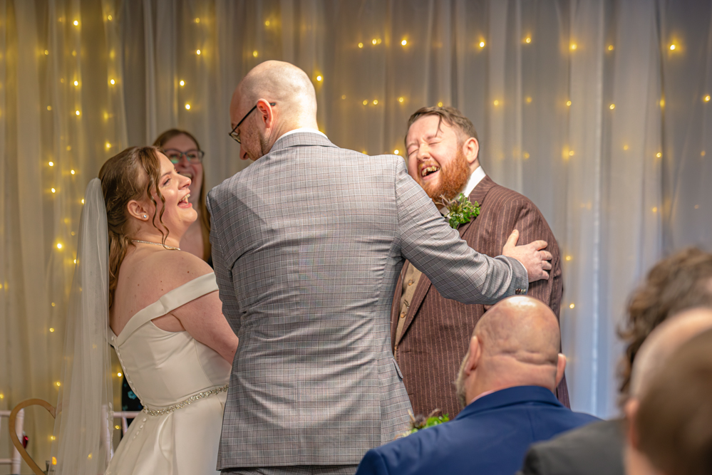 bride and groom laughing as brother of the bride gives his sister to the groom