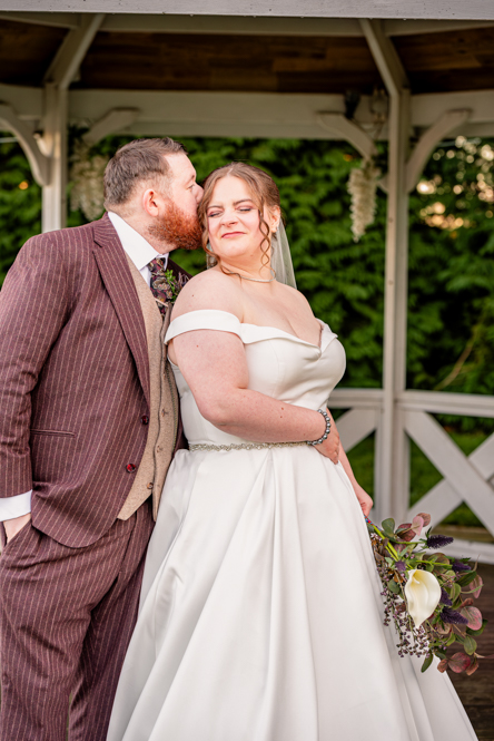 Groom kissing back of the brides head with bandstand behind them.