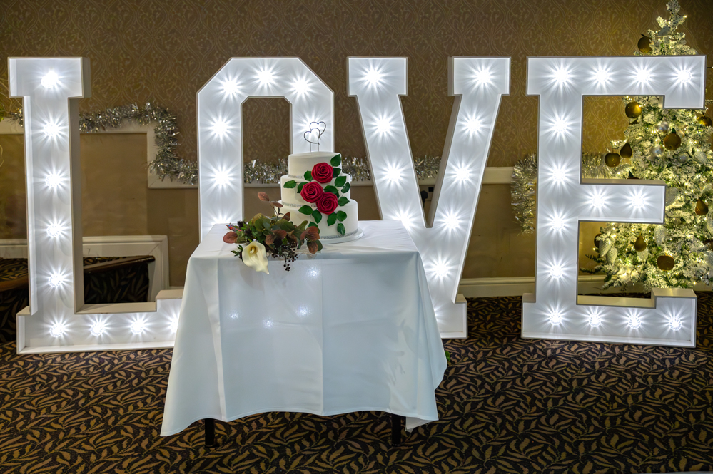 Large light-up Love letters behind wedding cake and brides bouquet