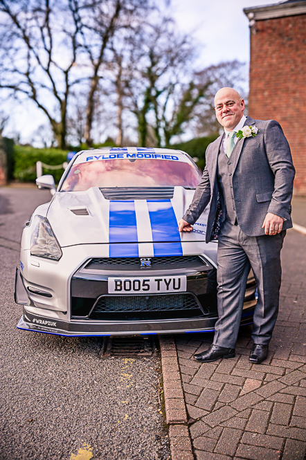 Groom with his arm on the bonnet of a grey with blue strips Nissan GT-R