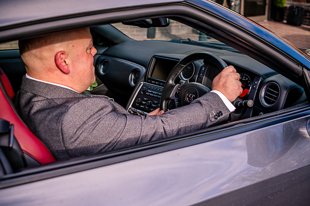 Close up of the Groom seating in the driving seat of a grey Nissan GT-R