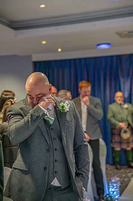 Groom wiping a tear away while waiting for bride to enter the room