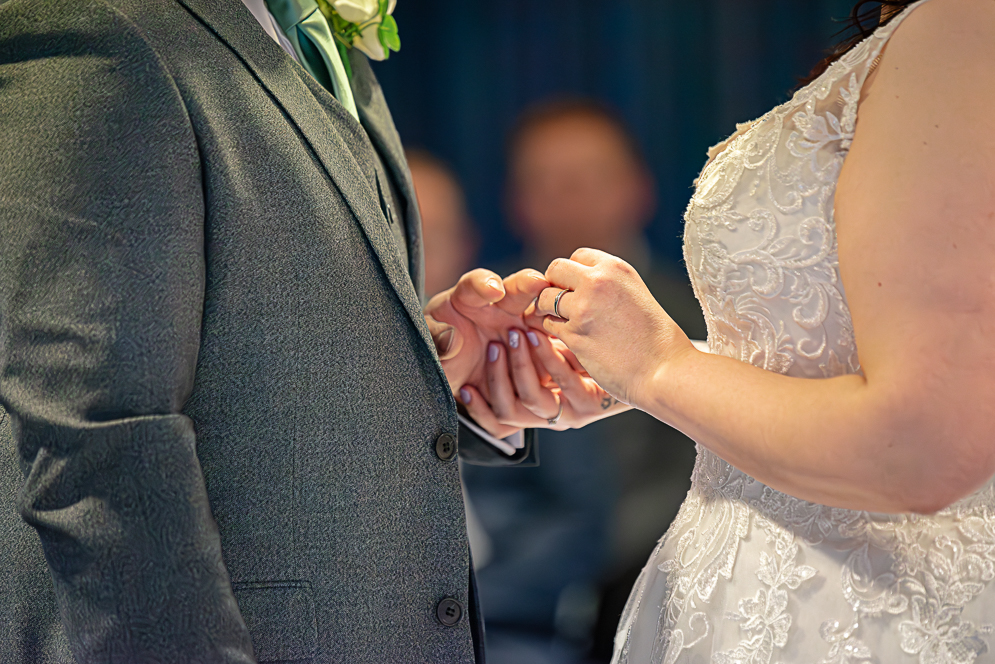 Bride putting the ring on grooms hand.