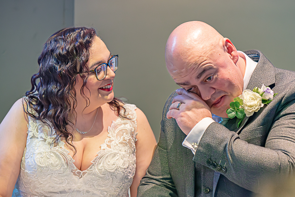 bride and groom seating at the wedding table after signing the register and groom wiping away a tear.