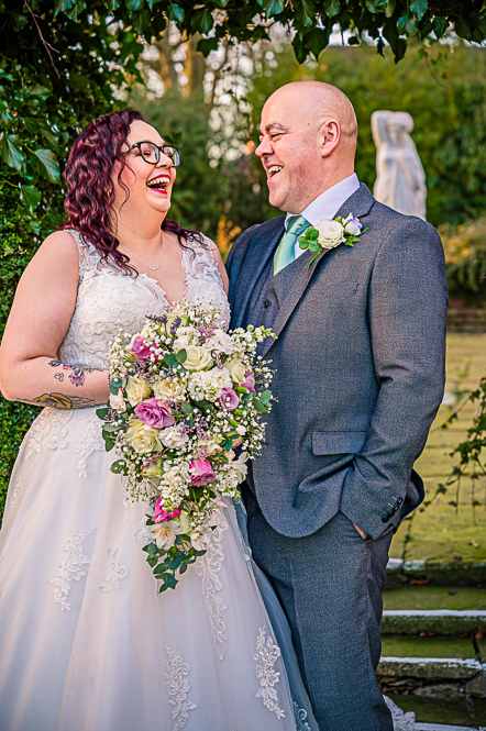 Bride and Groom laughing at each other with a leaf shaped arch behind them