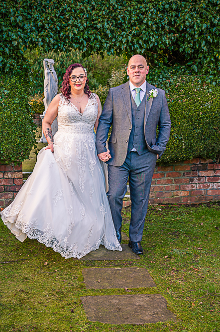 Bride and Groom walking while holding hands with a leaf shaped arch behind them