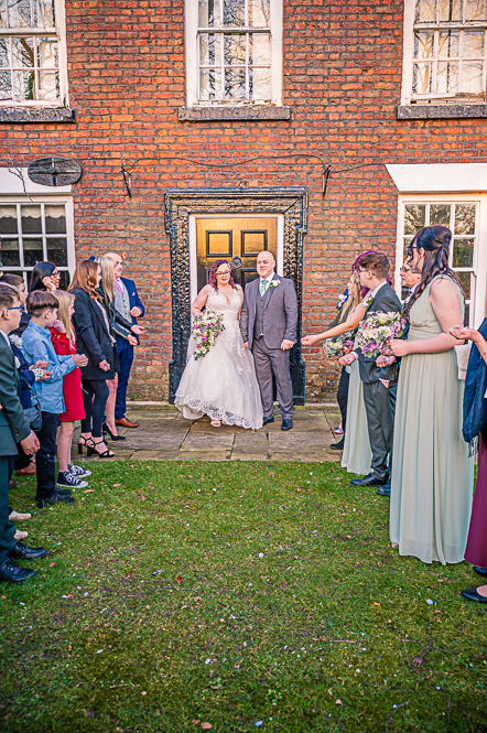 Bride and Groom and guests lining up for confetti to be thrown on them in front of a Georgian style building