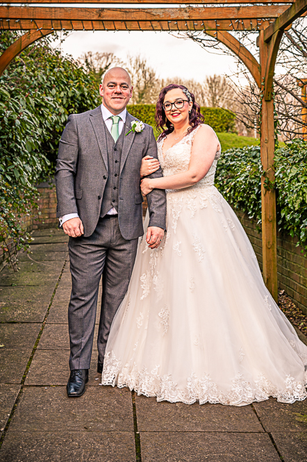 Bride and Groom standing under a gazebo with brides arms wrapped around grooms arm