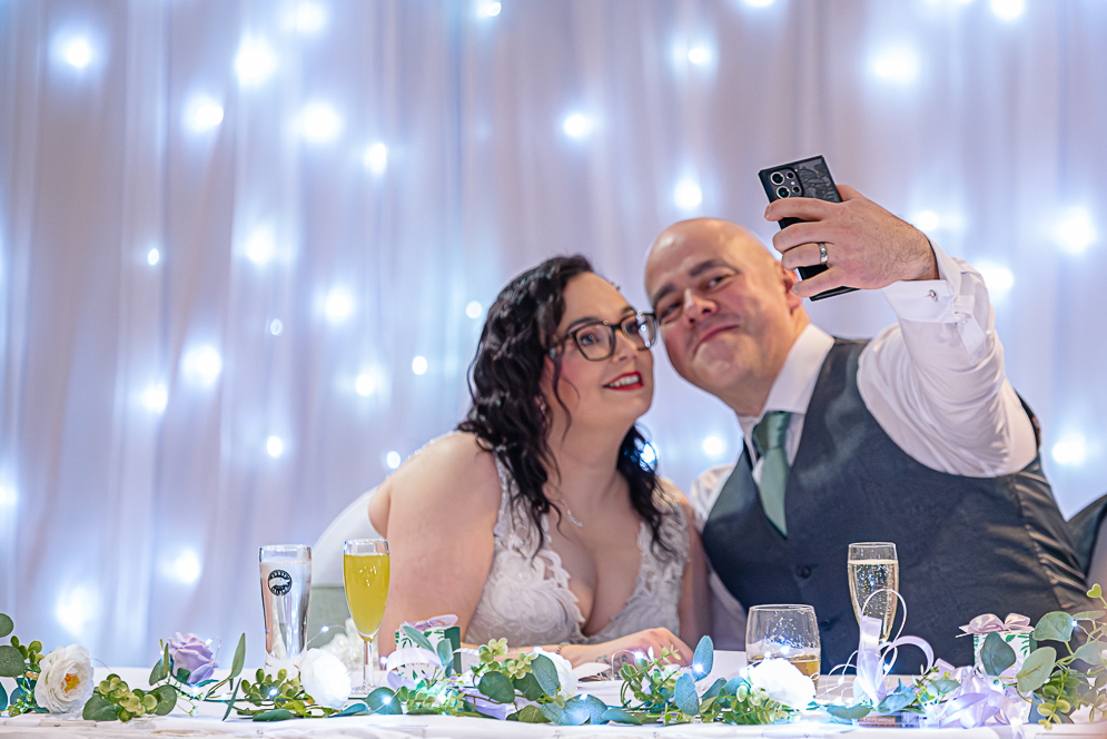 Bride and Groom taking a selfie while at the top table.