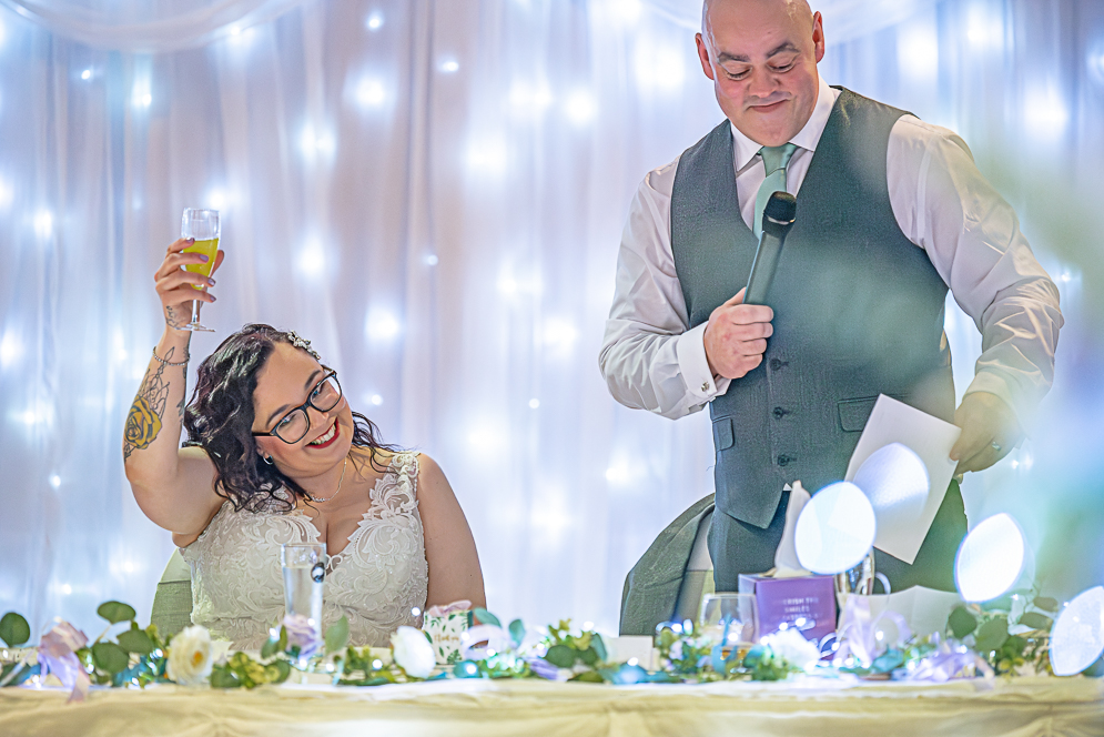 Groom’s speech and bride lifting up glass with smile