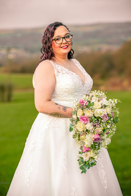 Side portrait of the bride holding her bouquet with the Greater Manchester hills behind her
