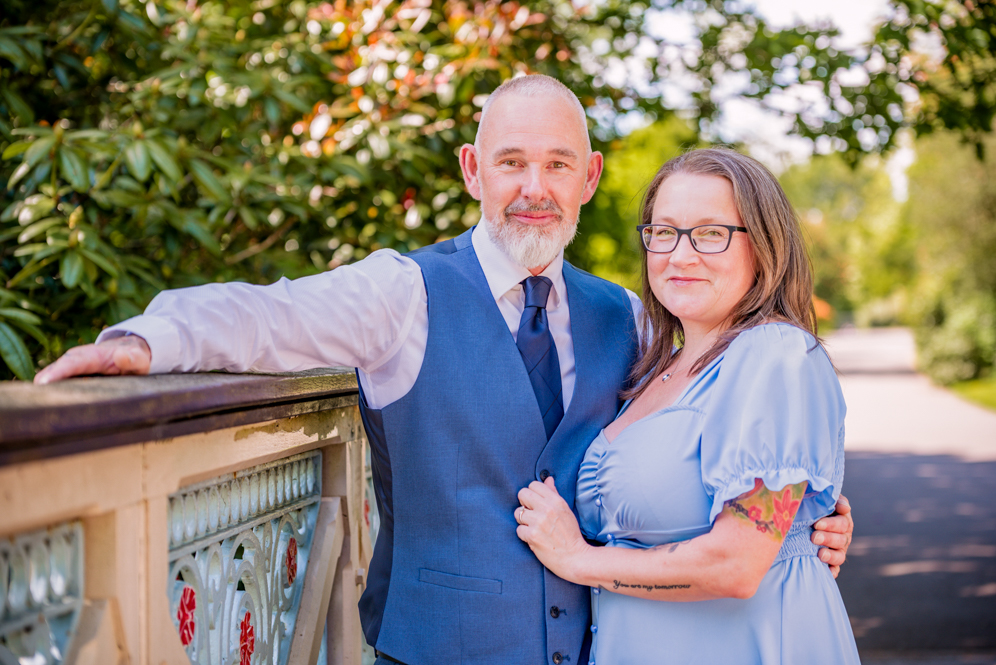 Couple standing together while man's arm is resting on the side of a bridge