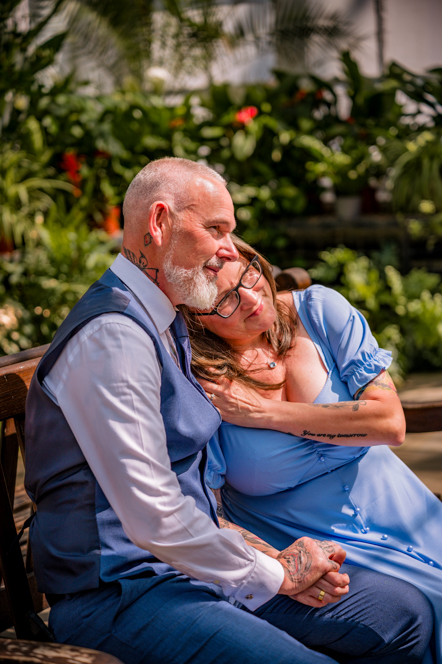 Lady resting head on man's shoulder and holding hands while sitting on a bench in a botanical gardens taken by Manchester Photographer Wedding Rebekah Morecroft