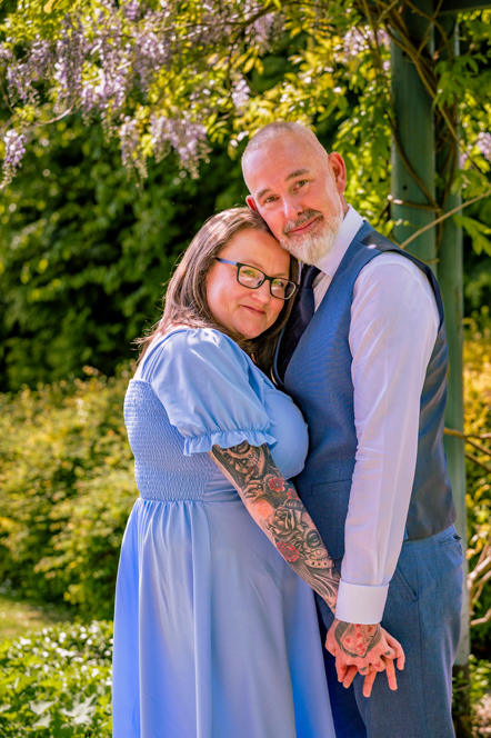 Side view of couple holding hands but facing the camera with Garden behind them